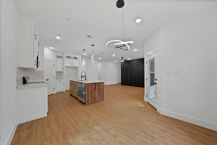 Kitchen with open floor plan, glass insert cabinets, decorative light fixtures, a center island with sink, and white cabinetry