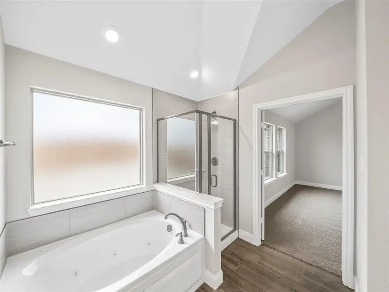 Full bath with vaulted ceiling, a tub with jets, wood finished floors, a stall shower, and baseboards