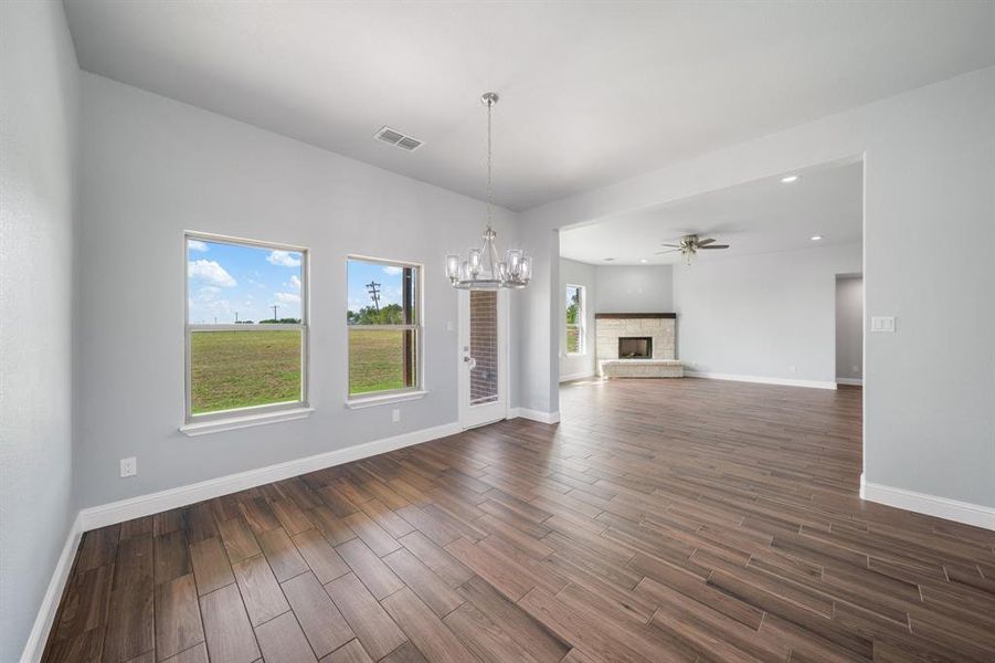 Unfurnished living room featuring a stone fireplace, ceiling fan with notable chandelier, and hardwood / wood-style floors