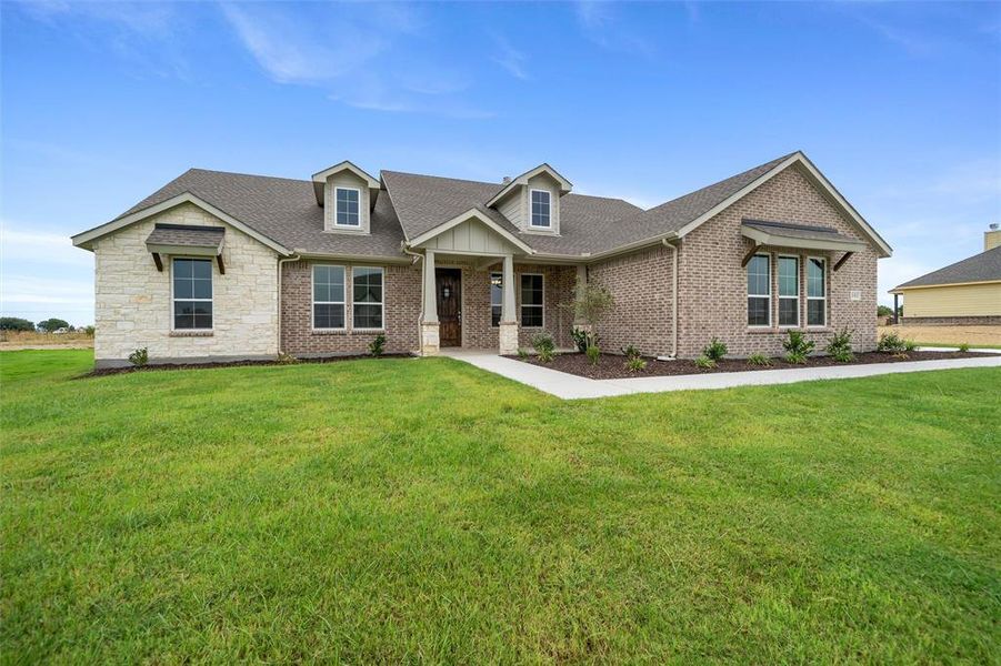 View of front of home featuring roof with shingles, a front lawn, stone siding, and brick siding