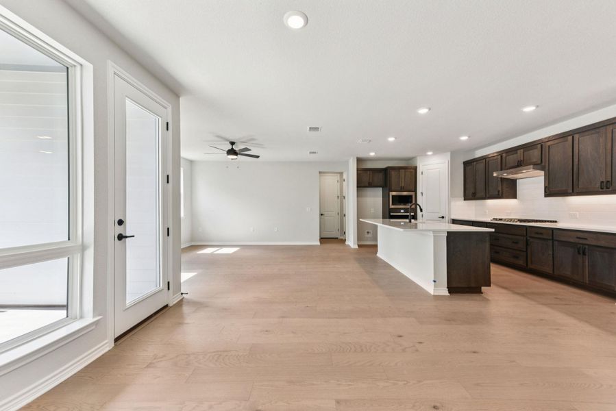 Kitchen with an island with sink, recessed lighting, dark brown cabinets, decorative backsplash, and light wood-type flooring