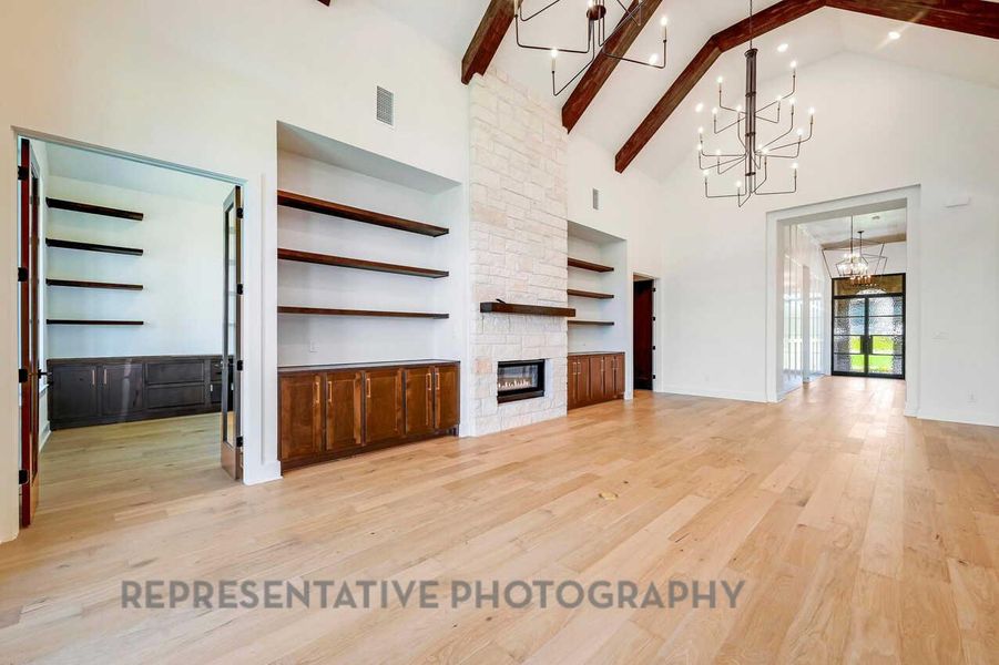 Unfurnished living room with high vaulted ceiling, light wood-style flooring, a fireplace, a chandelier, and beam ceiling Unfurnished living room with high vaulted ceiling, light wood-style flooring, a fireplace, a chandelier, and beam ceiling