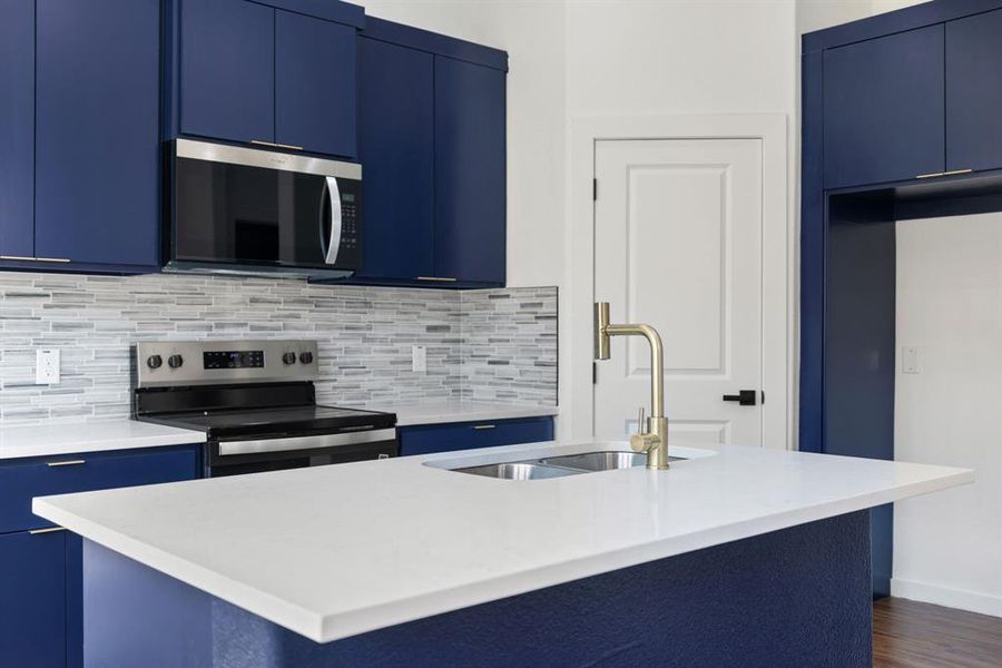 Kitchen featuring blue cabinets, stainless steel appliances, a kitchen island with sink, decorative backsplash, and light stone counters