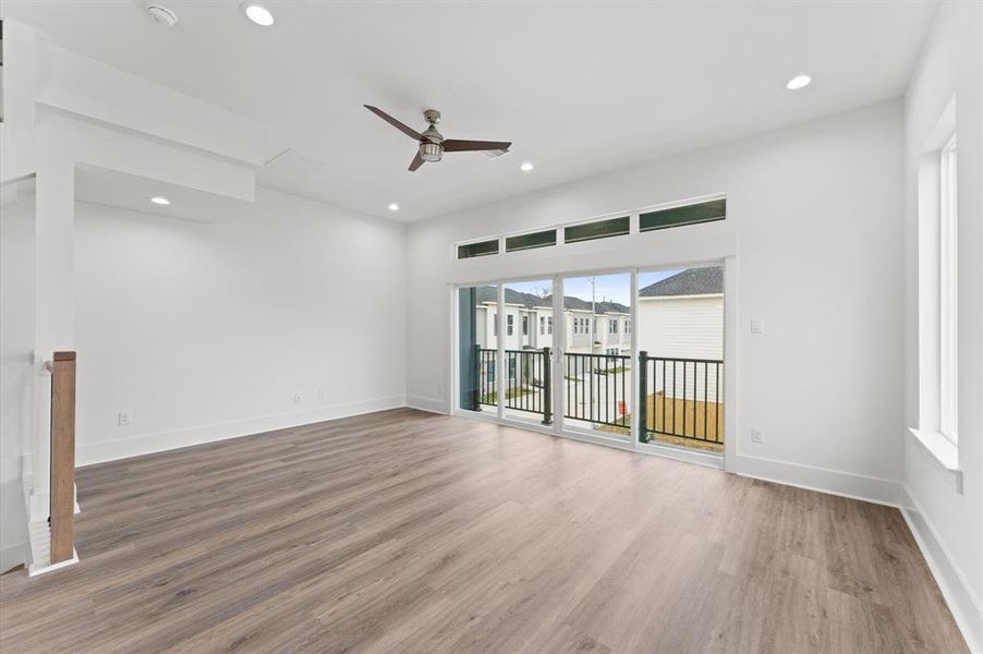 Bright and spacious living area with modern wood flooring, ceiling fan, and large windows leading to a balcony, perfect for natural light and outdoor views.