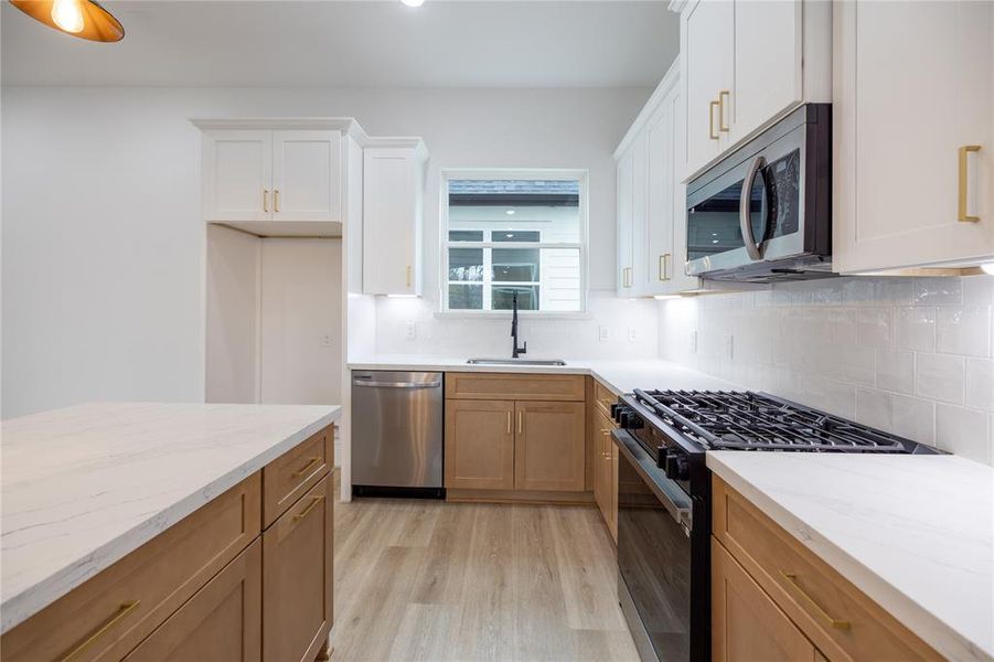 The natural wood cabinetry is thoughtfully complemented by white Calacatta quartz countertops and gold hardware. A sleek stainless steel farmhouse sink, paired with dark plumbing hardware, adds a modern, sophisticated touch to the space.