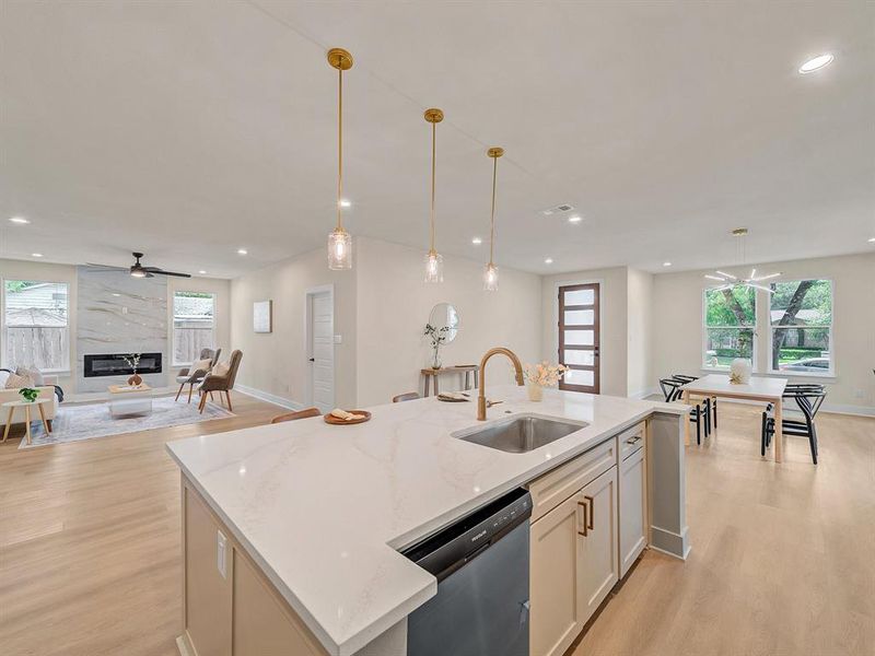 Kitchen with stainless steel dishwasher, decorative light fixtures, light stone countertops, and sink