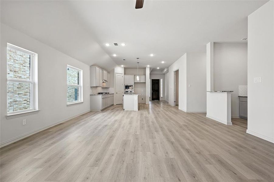 Unfurnished living room with light wood-type flooring, a ceiling fan, recessed lighting, and vaulted ceiling Unfurnished living room with light wood-type flooring, a ceiling fan, recessed lighting, and vaulted ceiling