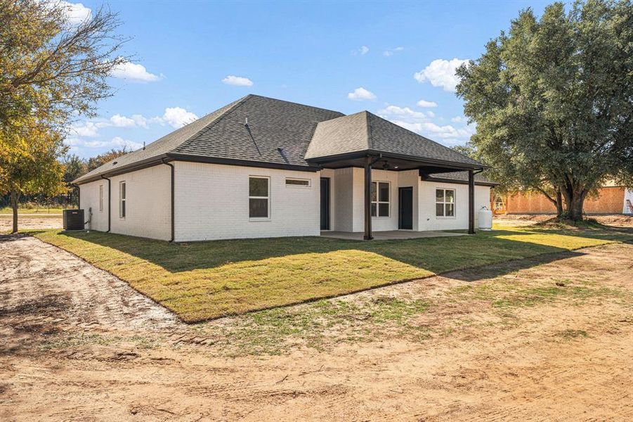 Back of house featuring brick siding, a patio, a lawn, and roof with shingles