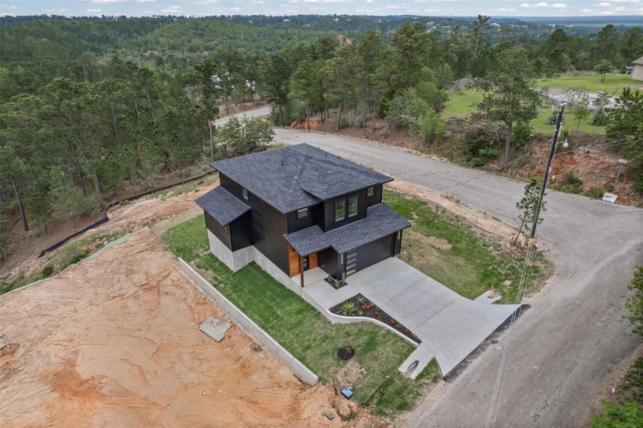 Contemporary home featuring dark siding, a dark shingle roof, and a concrete driveway on corner lot Contemporary home featuring dark siding, a dark shingle roof, and a concrete driveway on corner lot
