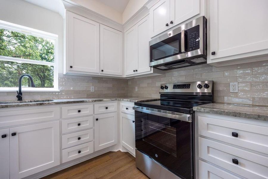 Kitchen with stainless steel appliances, white cabinets, light stone countertops, and dark wood-style flooring