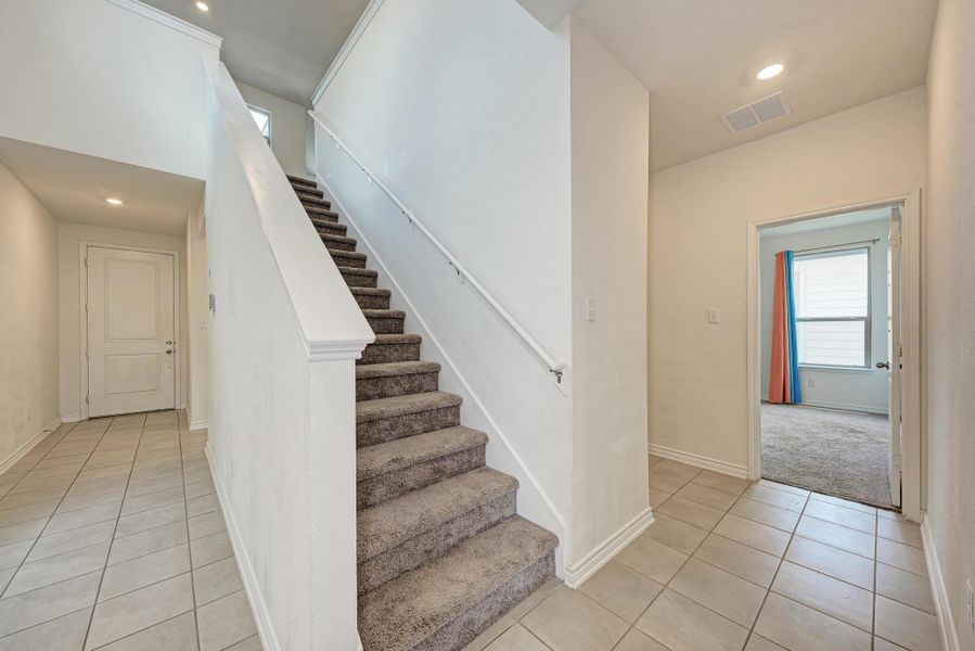 A well-lit entry hall with tile flooring transitions to a carpeted staircase leading to the upper level.