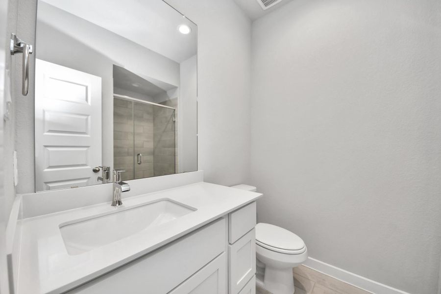 Secondary bath features tile flooring, walk-in shower with tile surround, light stained wood cabinets, beautiful light countertop. Sample photo of completed home with similar floor plan. Actual colors and selections may vary.