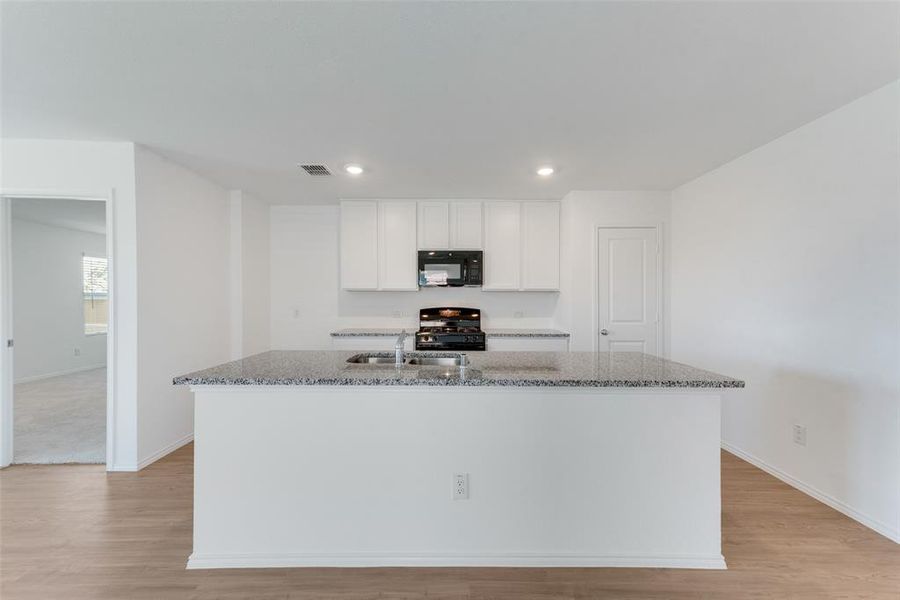 Kitchen with white cabinets, a kitchen island with sink, stone countertops, and black appliances