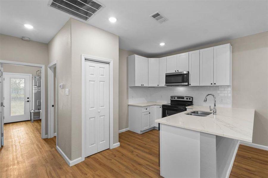 Kitchen with white cabinetry, black electric range oven, a peninsula, stainless steel microwave, and light stone counters