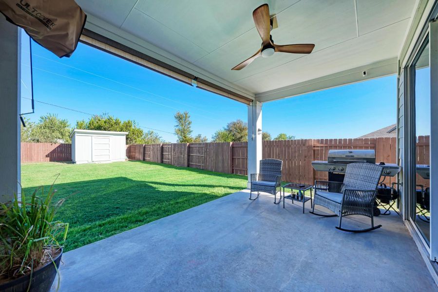 Fenced backyard with a ceiling fan, a patio, a storage shed, and grilling area
