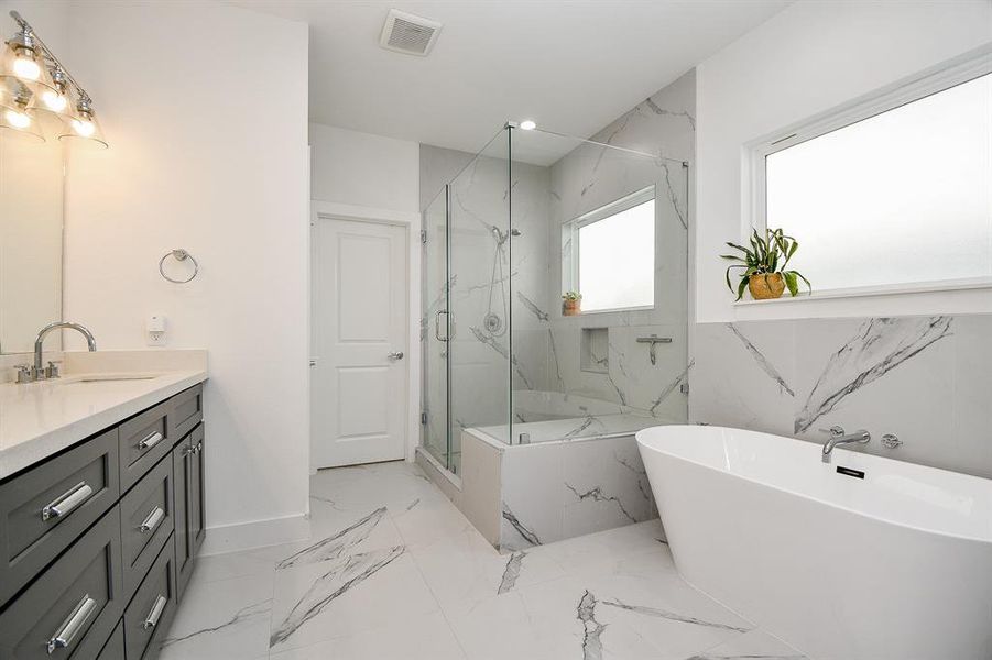 The primary bath has a freestanding soaking tub, a modern design glass-enclosed shower with marble patterned tiles.