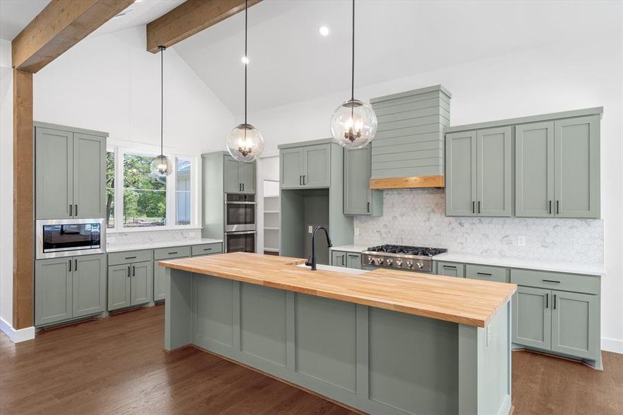 Kitchen with decorative light fixtures, backsplash, high vaulted ceiling, dark wood finished floors, and a kitchen island with sink Kitchen with decorative light fixtures, backsplash, high vaulted ceiling, dark wood finished floors, and a kitchen island with sink