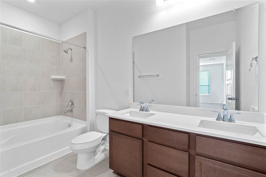 This move-in ready primary bathroom offers a spacious tub/shower combination with a tiled surround, stained cabinetry topped with light countertops, dual sinks, high ceilings, neutral paint, a large mirror, and sleek, modern finishes for a polished look.