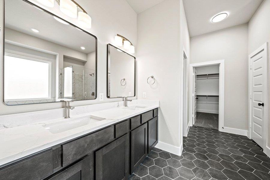 Full bathroom with double vanity, a shower stall, a walk in closet, and baseboards Full bathroom with double vanity, a shower stall, a walk in closet, and baseboards
