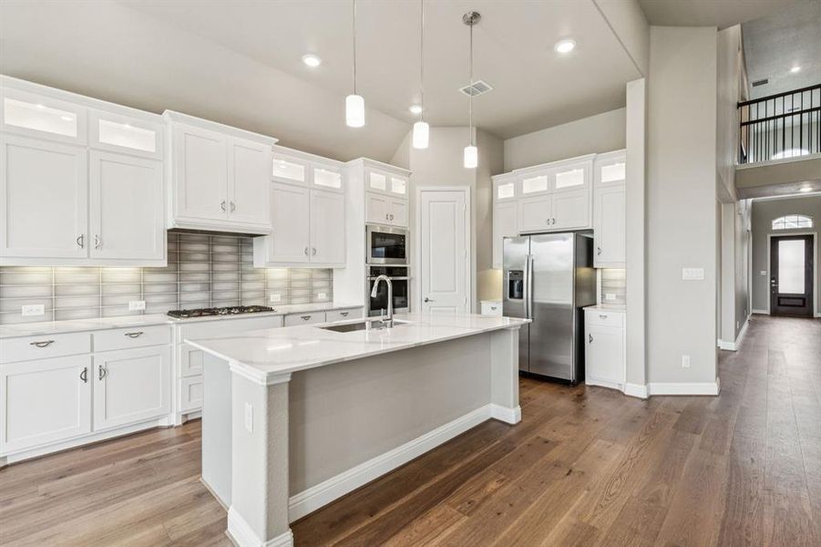 Kitchen featuring stainless steel appliances, backsplash, dark wood-style flooring, a kitchen island with sink, and white cabinetry