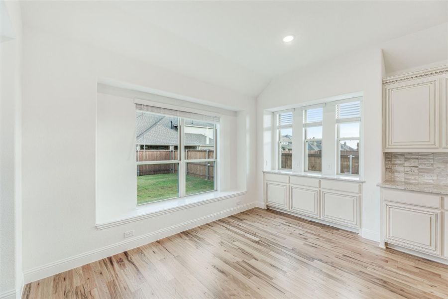 Bright dining area with light wood floors, large windows, and cream cabinets with tile backsplash