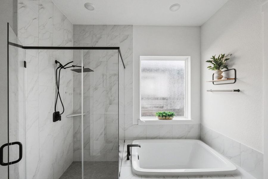 Spa-like primary bath featuring a freestanding soaking tub and oversized walk-in shower wrapped in marble-look tile. Matte black fixtures and soft natural light create a serene, modern sanctuary designed for relaxation.