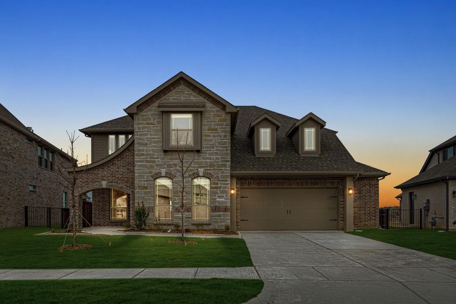 Two-story brick and stone home with two-car garage, arched entry, and front lawn at dusk Two-story brick and stone home with two-car garage, arched entry, and front lawn at dusk