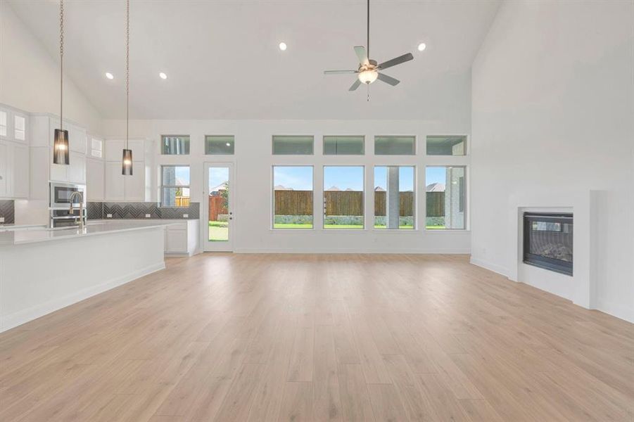 Spacious open-concept interior featuring light wood-finish flooring, a contemporary fireplace, and a vaulted ceiling with a ceiling fan Spacious open-concept interior featuring light wood-finish flooring, a contemporary fireplace, and a vaulted ceiling with a ceiling fan