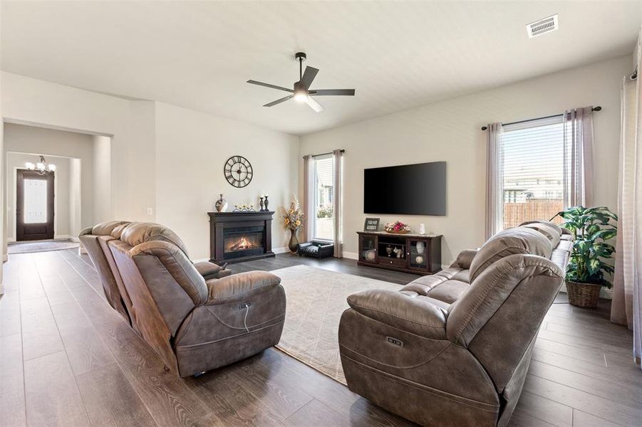 Spacious living area featuring wood-finish flooring, an electric fireplace with a dark mantel, and a ceiling fan with integrated lighting Spacious living area featuring wood-finish flooring, an electric fireplace with a dark mantel, and a ceiling fan with integrated lighting