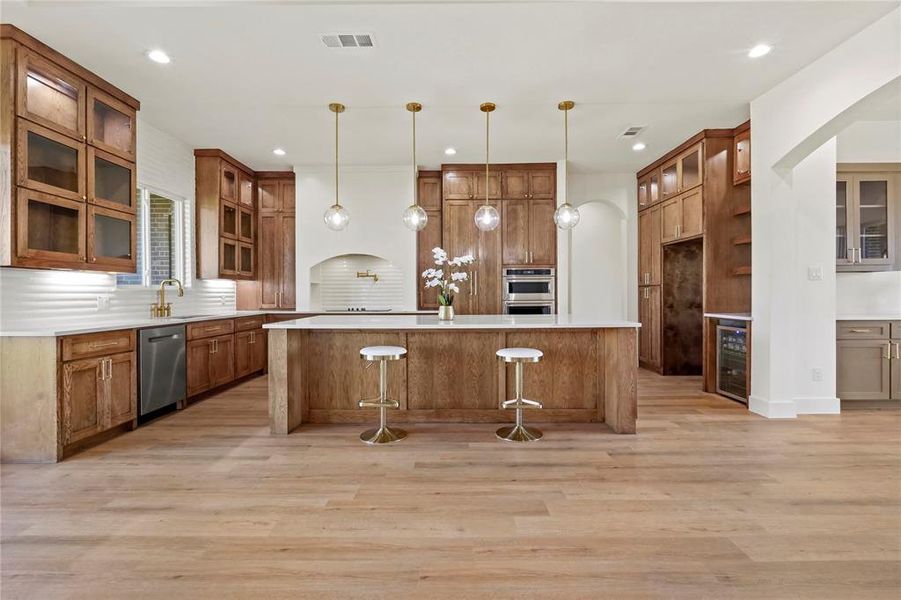 Kitchen featuring glass insert cabinets, brown cabinetry, a kitchen bar, and recessed lighting Kitchen featuring glass insert cabinets, brown cabinetry, a kitchen bar, and recessed lighting