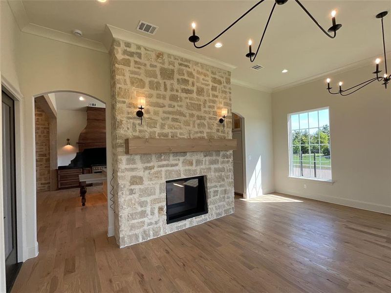 Unfurnished living room featuring a notable chandelier, a stone fireplace, ornamental molding, and hardwood / wood-style floors