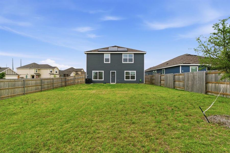 The property features a spacious rear yard with a green lawn and a wooden privacy fence