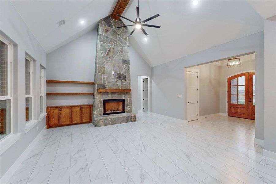 Unfurnished living room featuring high vaulted ceiling, beamed ceiling, ceiling fan with notable chandelier, and a fireplace