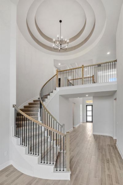 Stairway with a tray ceiling, recessed lighting, wood finished floors, and a chandelier