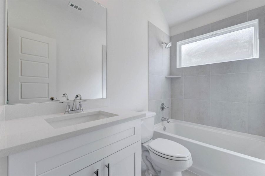 Secondary bathroom with white vanity, chrome fixtures, large mirror, tub/shower combination, neutral tile surround, and frosted privacy window. The clean, light finishes create a fresh new-construction feel, while the full bath layout offers practical everyday function for guests or secondary bedrooms.
