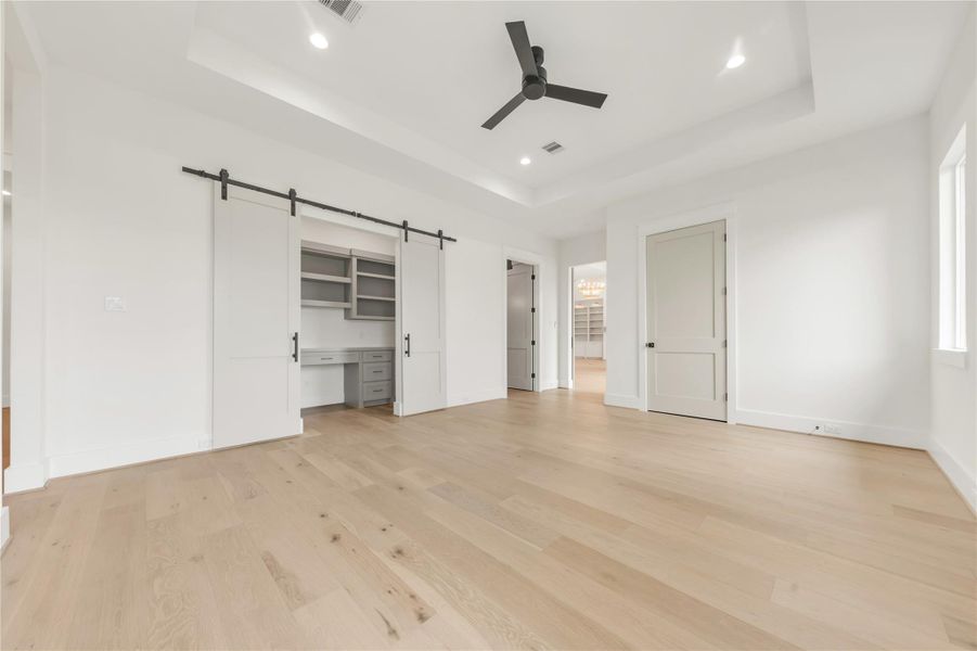 Unfurnished bedroom with a barn door, a tray ceiling, light wood-style flooring, a walk in closet, and recessed lighting