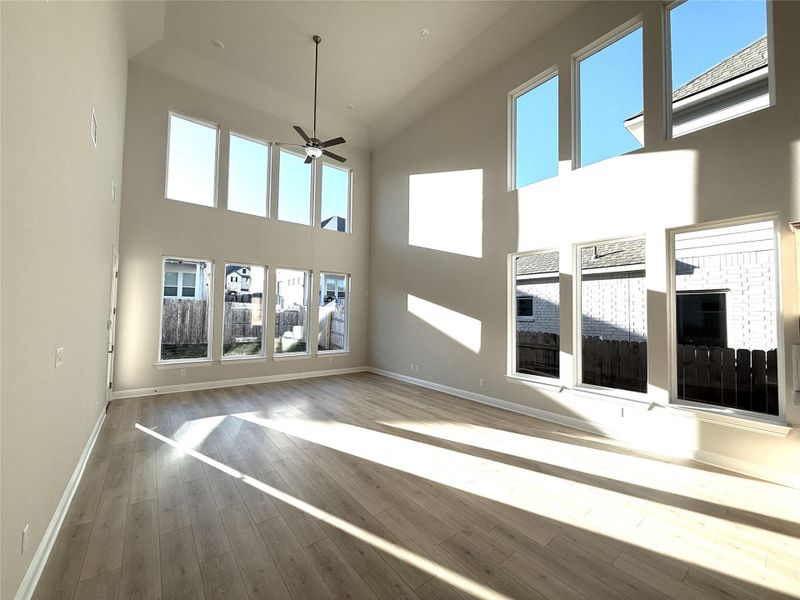 Unfurnished living room with a ceiling fan, light wood-style floors, and a towering ceiling