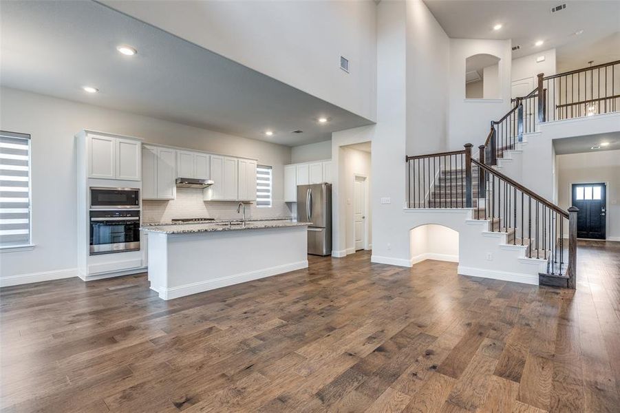 Kitchen with appliances with stainless steel finishes, white cabinets, a sink, dark wood-style flooring, and a towering ceiling