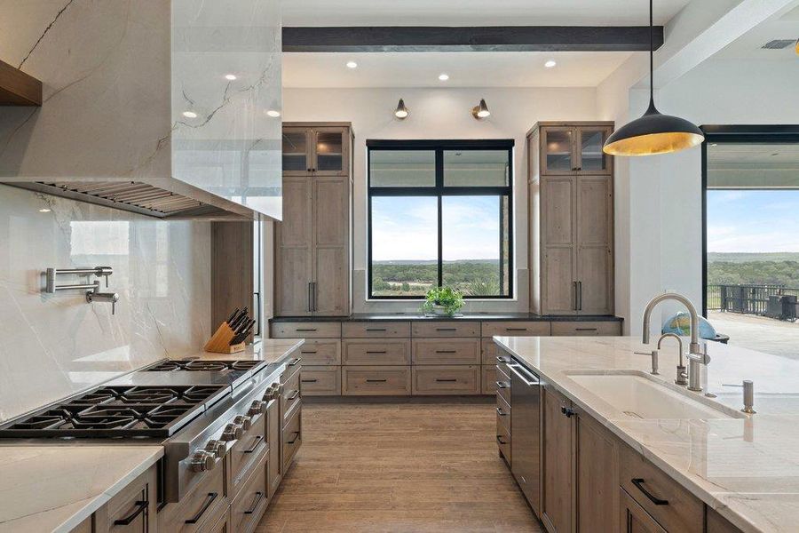 Gourmet kitchen featuring a large gas range with a pot filler, custom range hood, and light wood-finish cabinetry