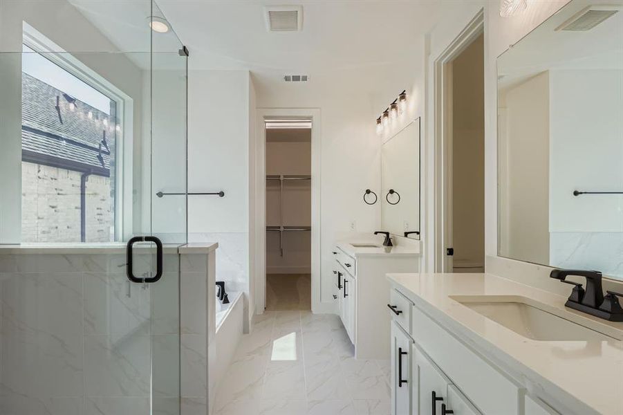 Full bathroom featuring a spacious closet, two vanities, a shower stall, light marble finish flooring, and a tub Full bathroom featuring a spacious closet, two vanities, a shower stall, light marble finish flooring, and a tub