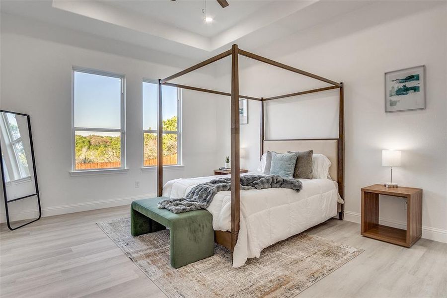 Bedroom with light wood finished floors, ceiling fan, and a raised ceiling Bedroom with light wood finished floors, ceiling fan, and a raised ceiling