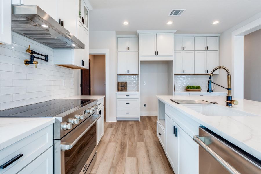 Kitchen with stainless steel appliances, light stone counters, light wood-style flooring, white cabinetry, and backsplash