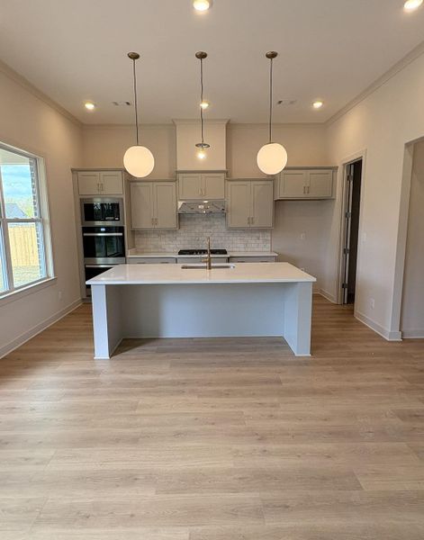 Kitchen with gray cabinets, decorative light fixtures, a kitchen island with sink, light wood-style flooring, and a kitchen bar