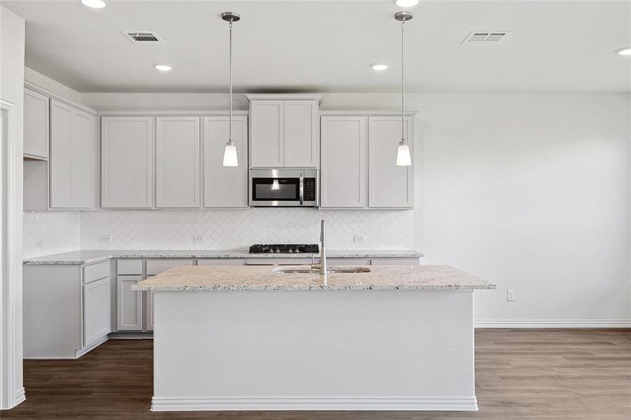 Kitchen with light stone countertops, hardwood / wood-style floors, tasteful backsplash, sink, and a kitchen island with sink