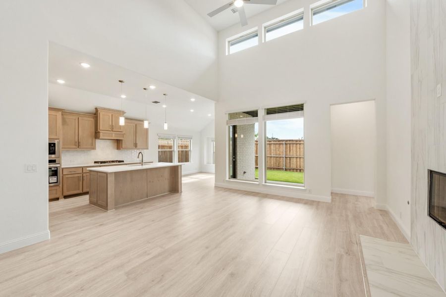 Open-concept living area and kitchen with high ceilings, light wood floors, and large windows