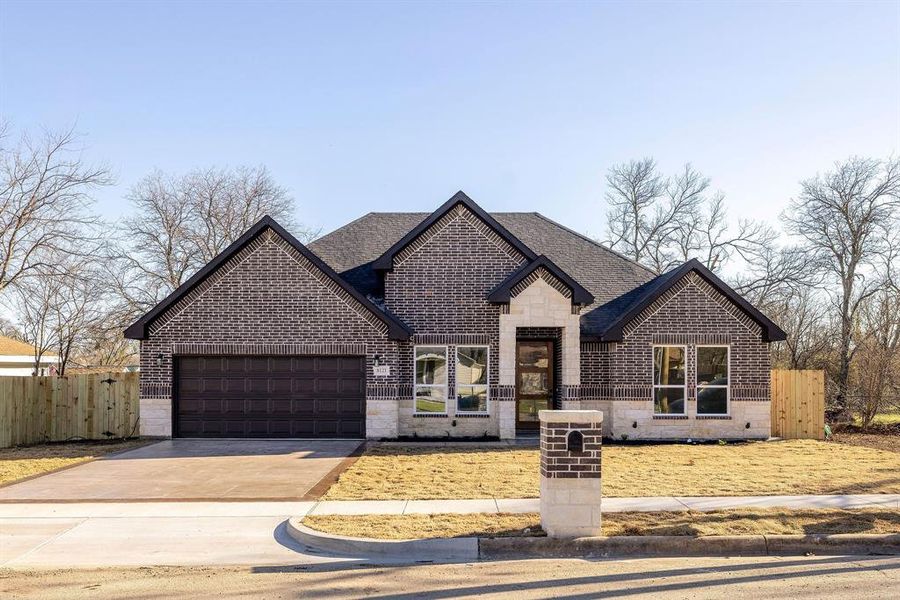 French country inspired facade featuring stone siding, fence, concrete driveway, and brick siding