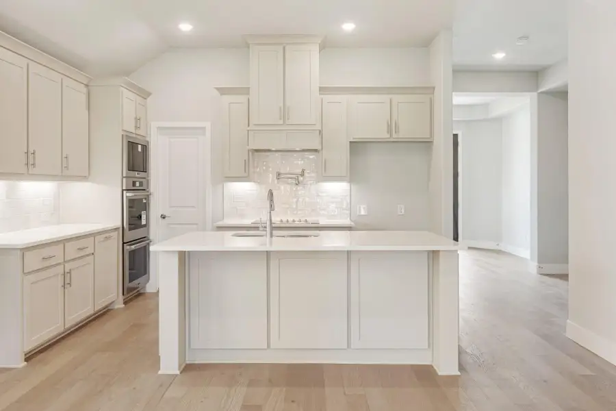 Kitchen with large center island, white cabinets, tile backsplash, and light hardwood floors