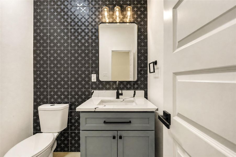 Chic powder room featuring a modern vanity with a sleek quartz countertop, stylish black tile accent wall, and elegant lighting fixtures.