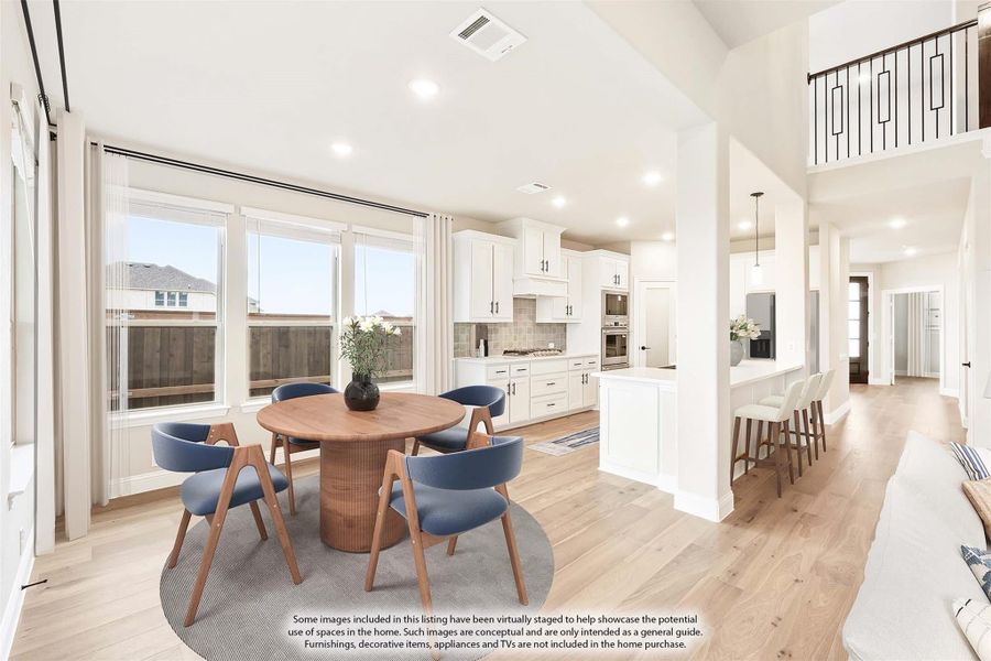 Open-concept dining area with round wood table, blue chairs, and white kitchen with high ceilings and hardwood floors