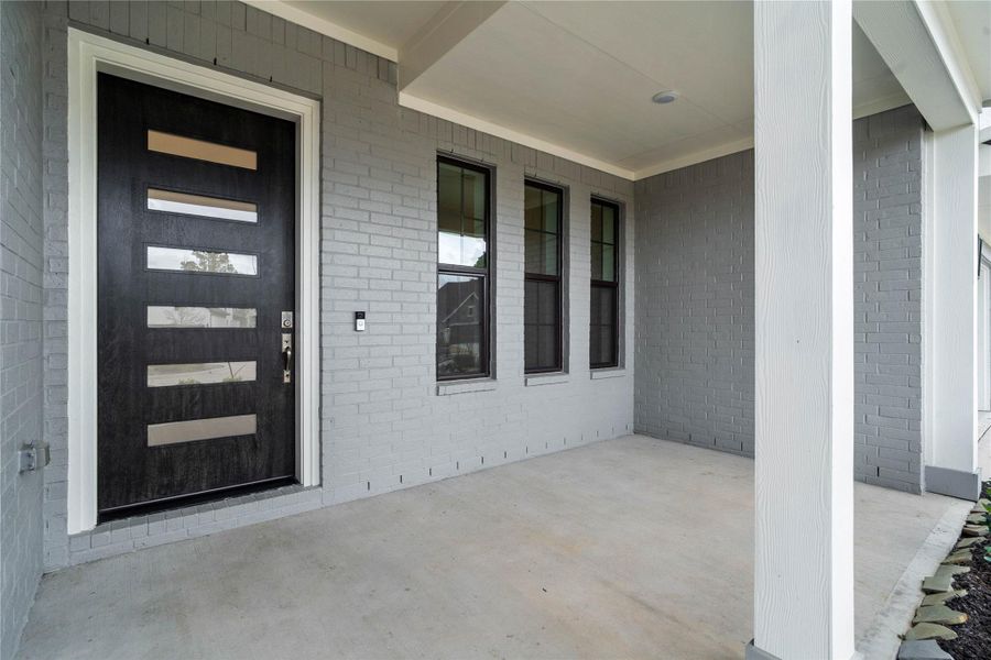 This covered front porch offers a clean, contemporary feel with its sleek grey brick façade and smooth concrete flooring. The space is anchored by a stunning modern five-lite glass front door in a rich dark finish, which provides an inviting and sophisticated entrance to the home. This covered front porch offers a clean, contemporary feel with its sleek grey brick façade and smooth concrete flooring. The space is anchored by a stunning modern five-lite glass front door in a rich dark finish, which provides an inviting and sophisticated entrance to the home.